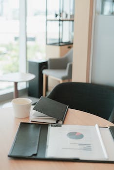 pexels-photo-10041250-10041250 A modern office setting featuring a notebook, coffee cup, and documents on a wooden desk.